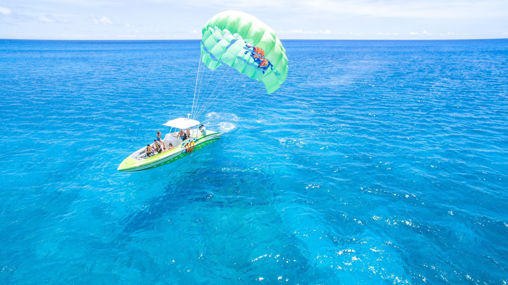 Person parasailing behind a boat over bright blue ocean