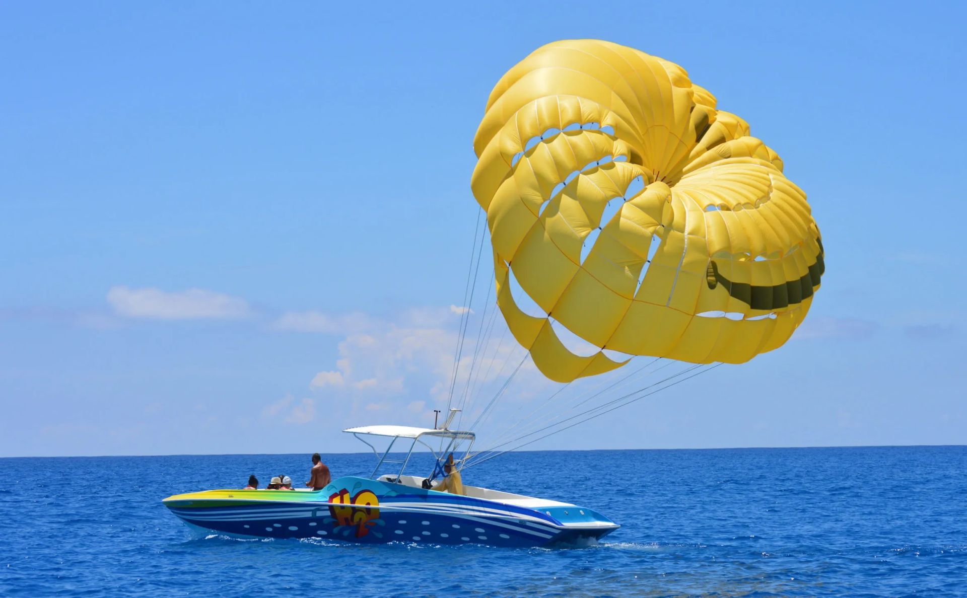 Yellow parasail above a blue speedboat on a calm ocean under a clear sky