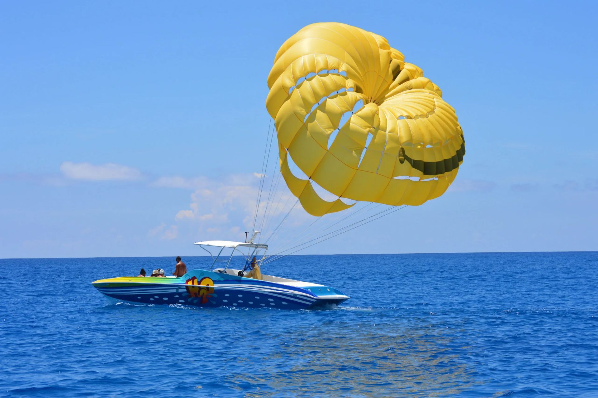 Yellow parasail above a blue boat on the ocean under a clear sky