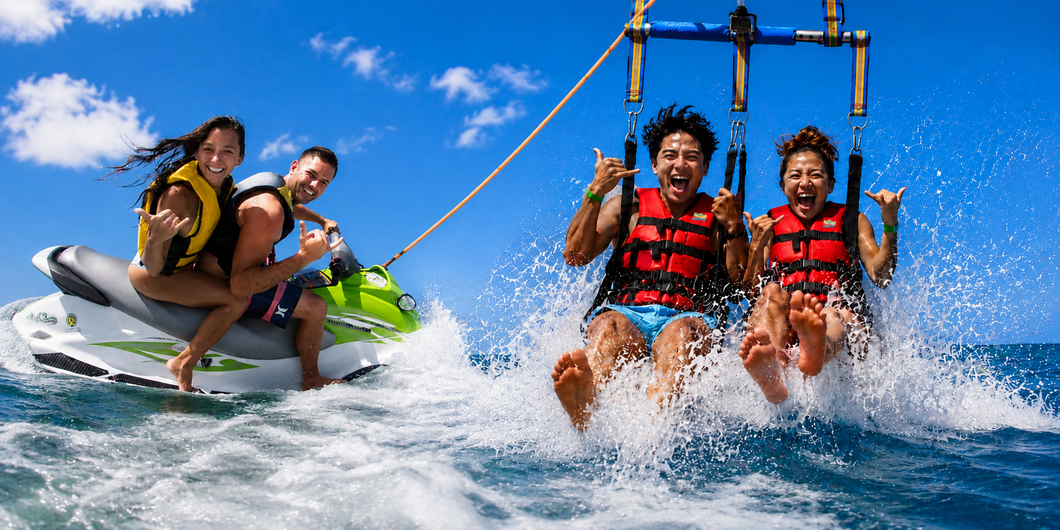 Two people on a jet ski and two peopele riding a parasail, smiling and splashing under a bright blue sky.