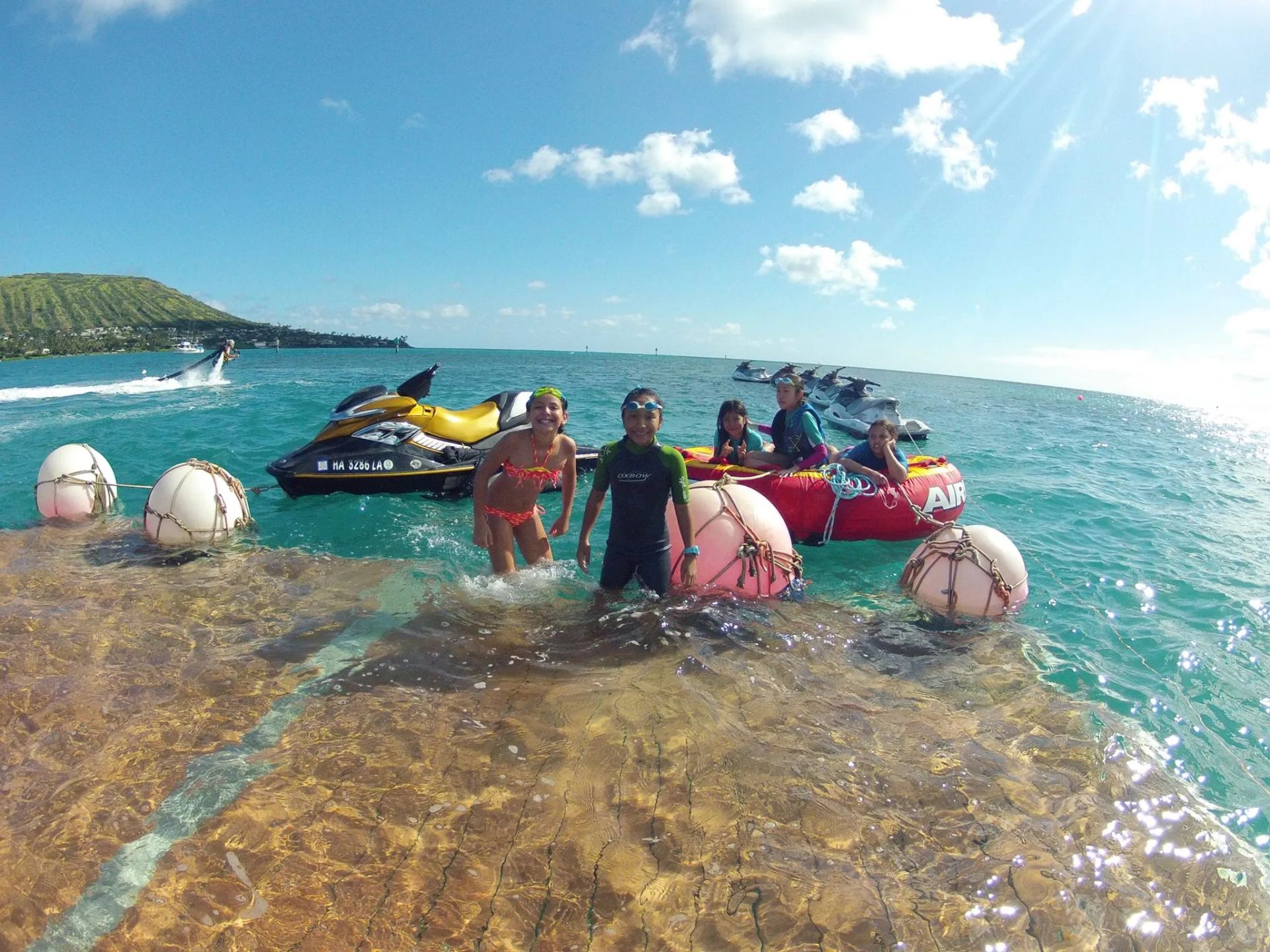 People hanging out in the water with jet skis and tubes in turquoise water
