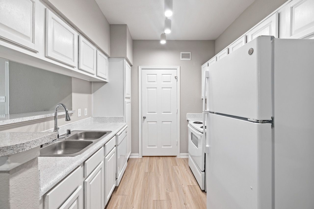 Galley-style kitchen with white cabinets, light countertops, double sink, and full-size appliances.