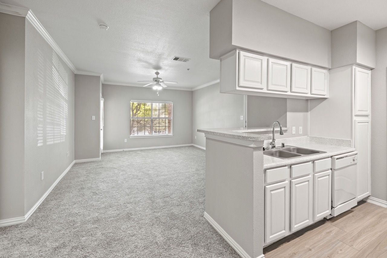 Open-concept kitchen with white cabinets and a peninsula sink, adjacent living area with window.