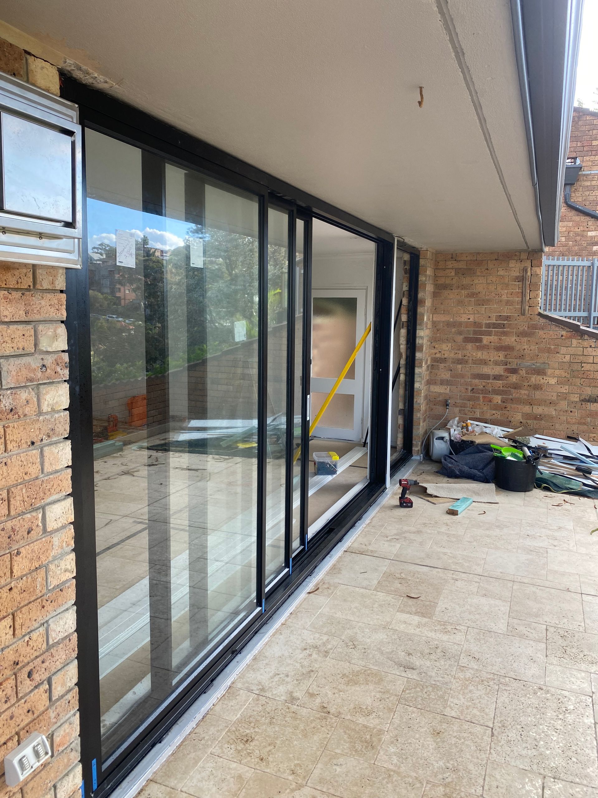 Exterior patio with sliding glass doors beside a brick wall and construction materials on the ground. — Kracken Windows and Doors In Terrey Hills, NSW