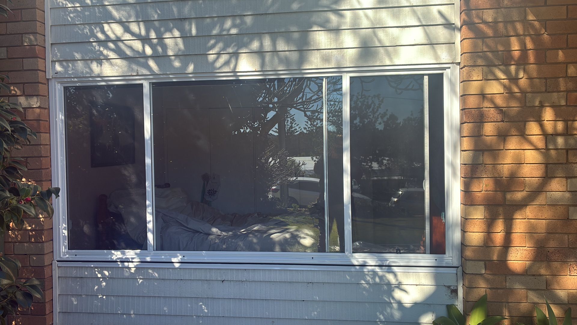 White-framed sliding window on a brick-and-siding house, with tree shadows across the glass. — Kracken Windows and Doors In Terrey Hills, NSW