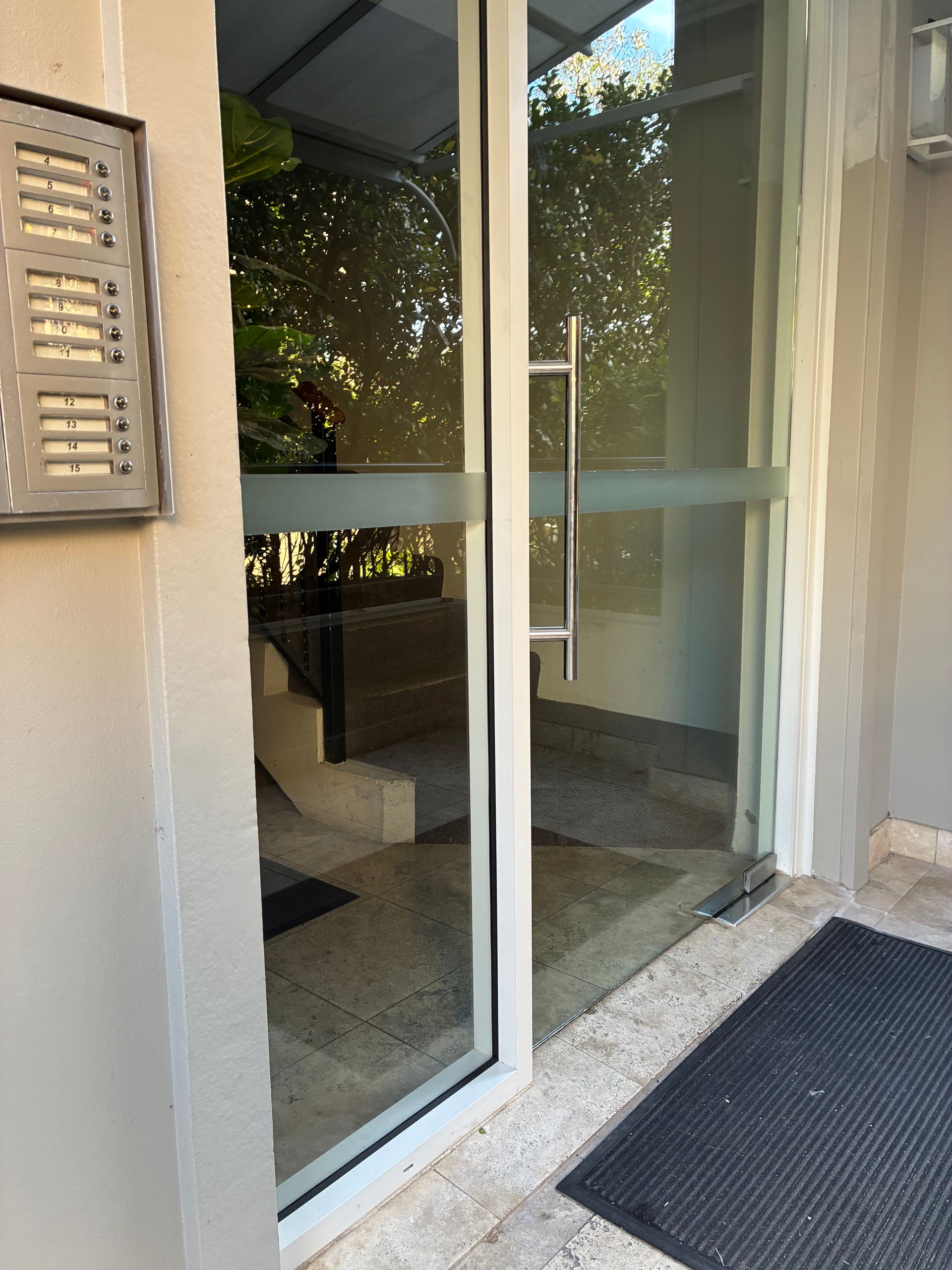 Glass apartment entrance door with black doormat and window blinds beside it — Kracken Windows and Doors In Terrey Hills, NSW