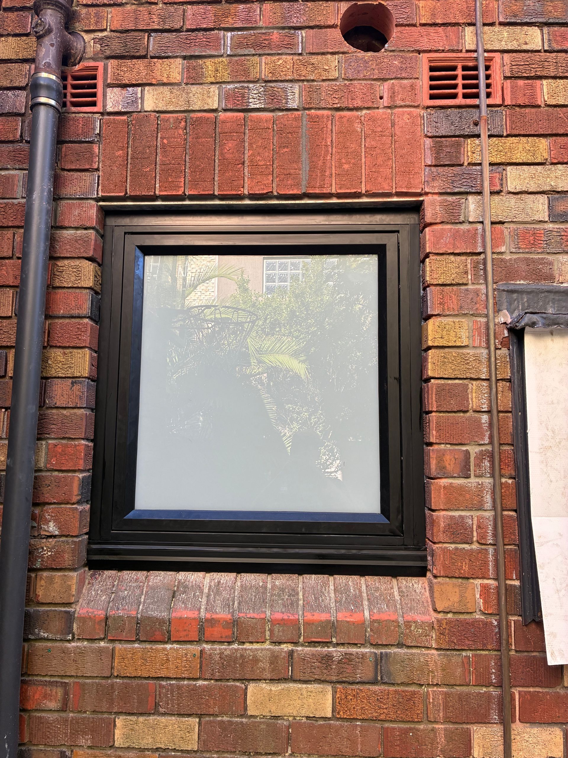 Brick building wall with a black-framed window reflecting trees and sky — Kracken Windows and Doors In Terrey Hills, NSW