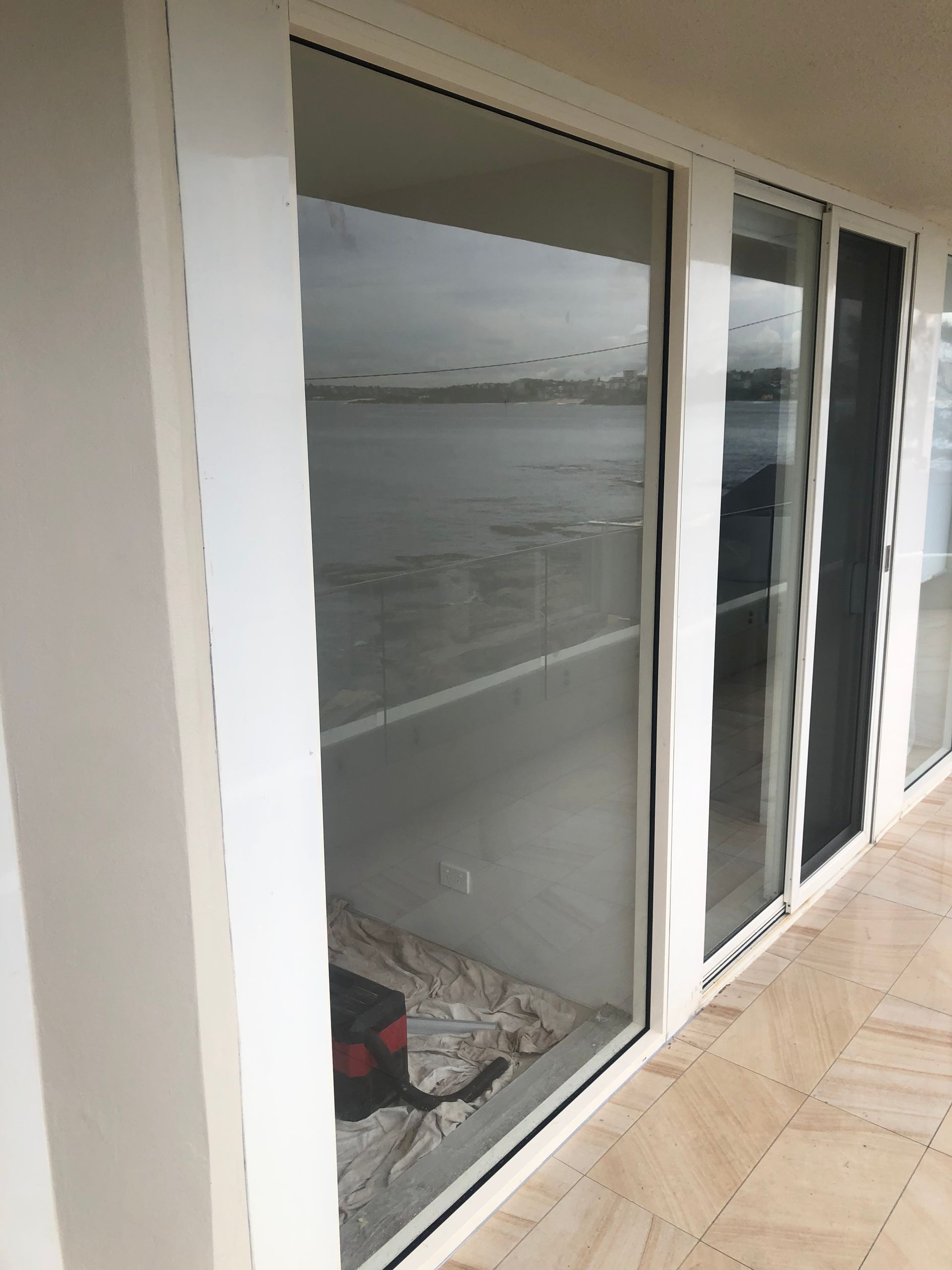 Glass sliding doors overlooking a calm waterfront, with tiled patio and white exterior wall — Kracken Windows and Doors In Terrey Hills, NSW