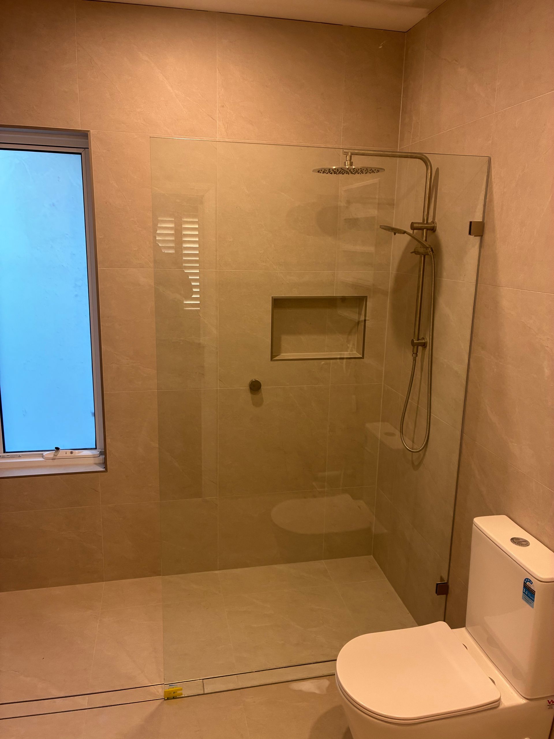 Modern beige bathroom with glass shower, wall shelf, and white toilet. — Kracken Windows and Doors In Terrey Hills, NSW
