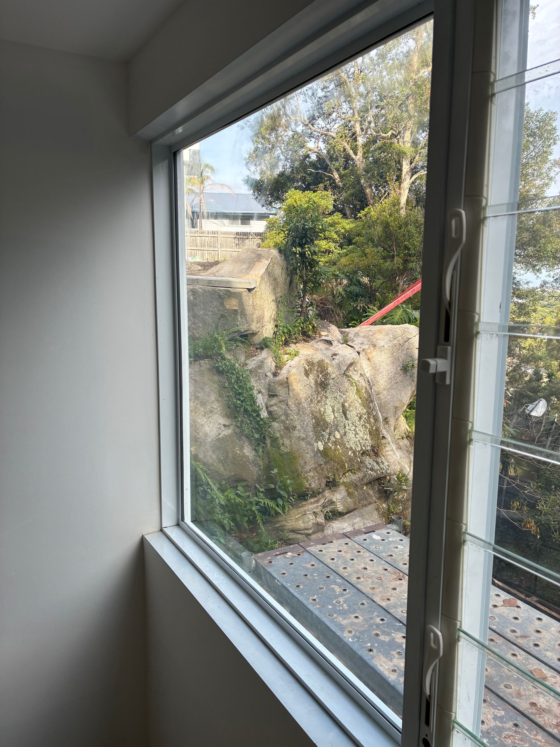 View through a window to a rocky hillside with greenery and a red railing outside — Kracken Windows and Doors In Terrey Hills, NSW