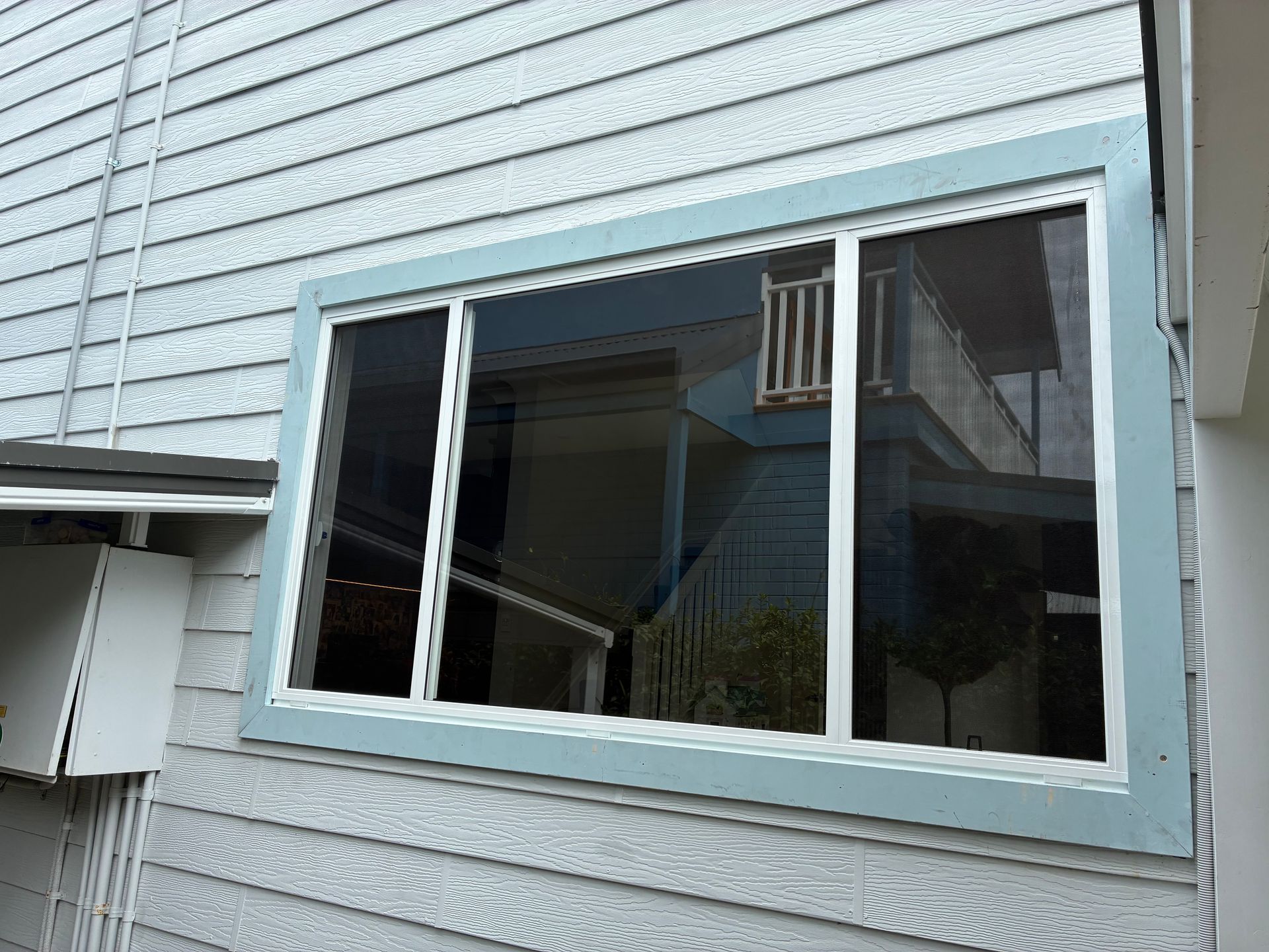 Blue house siding with a large window reflecting a porch and stair railing — Kracken Windows and Doors In Terrey Hills, NSW