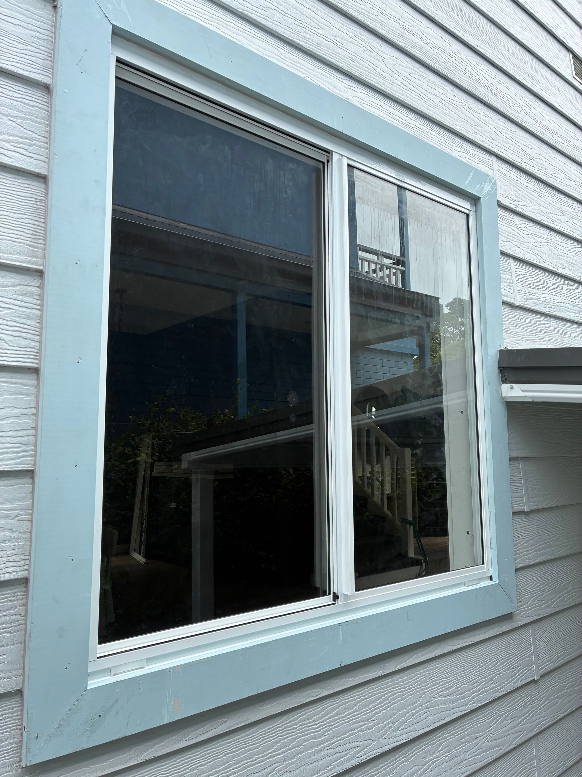 White-framed double window in a gray vinyl-sided exterior wall with reflections in the glass — Kracken Windows and Doors In Terrey Hills, NSW