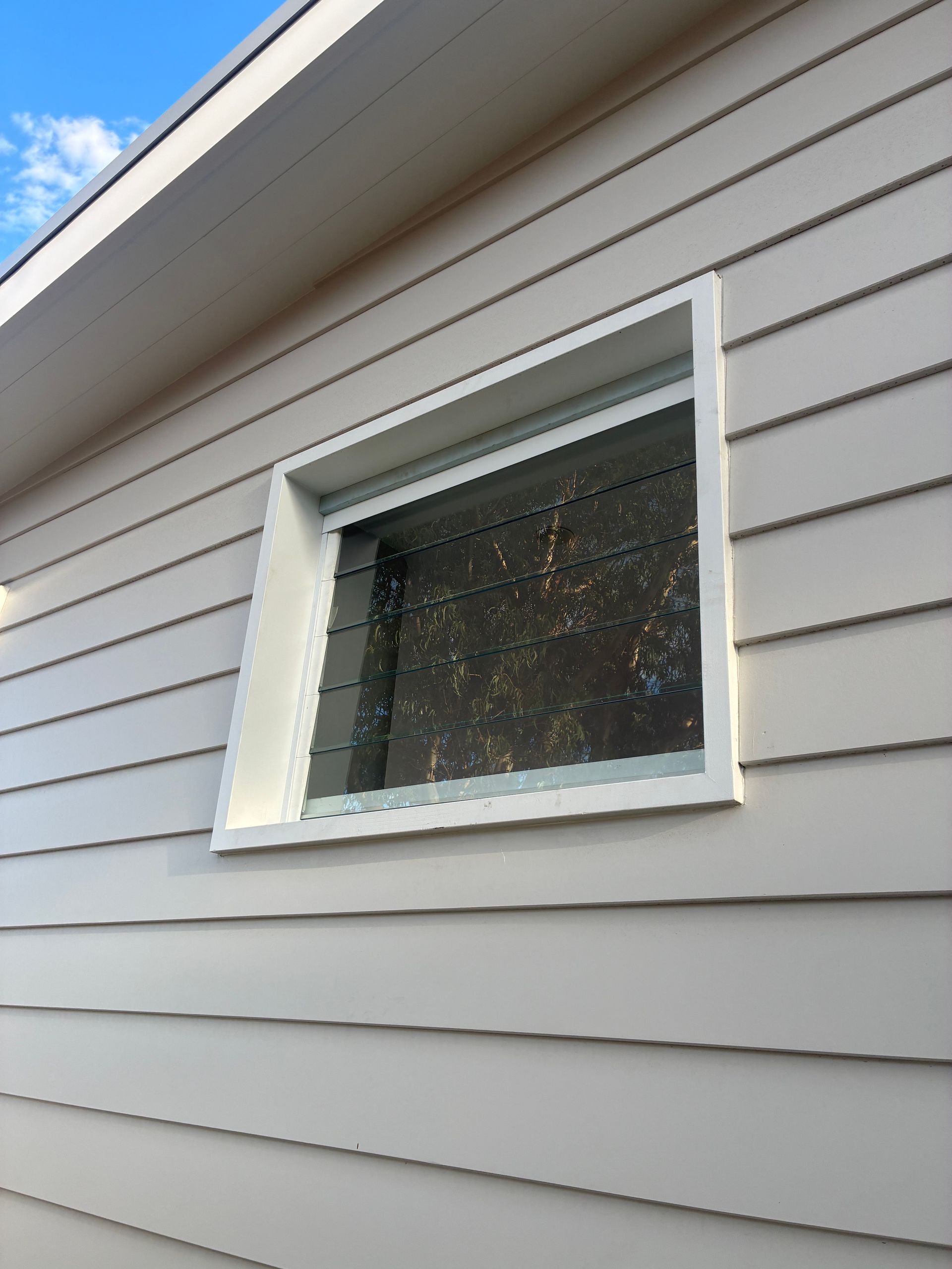 White-framed window on gray vinyl siding of a house, viewed at an angle. — Kracken Windows and Doors In Terrey Hills, NSW