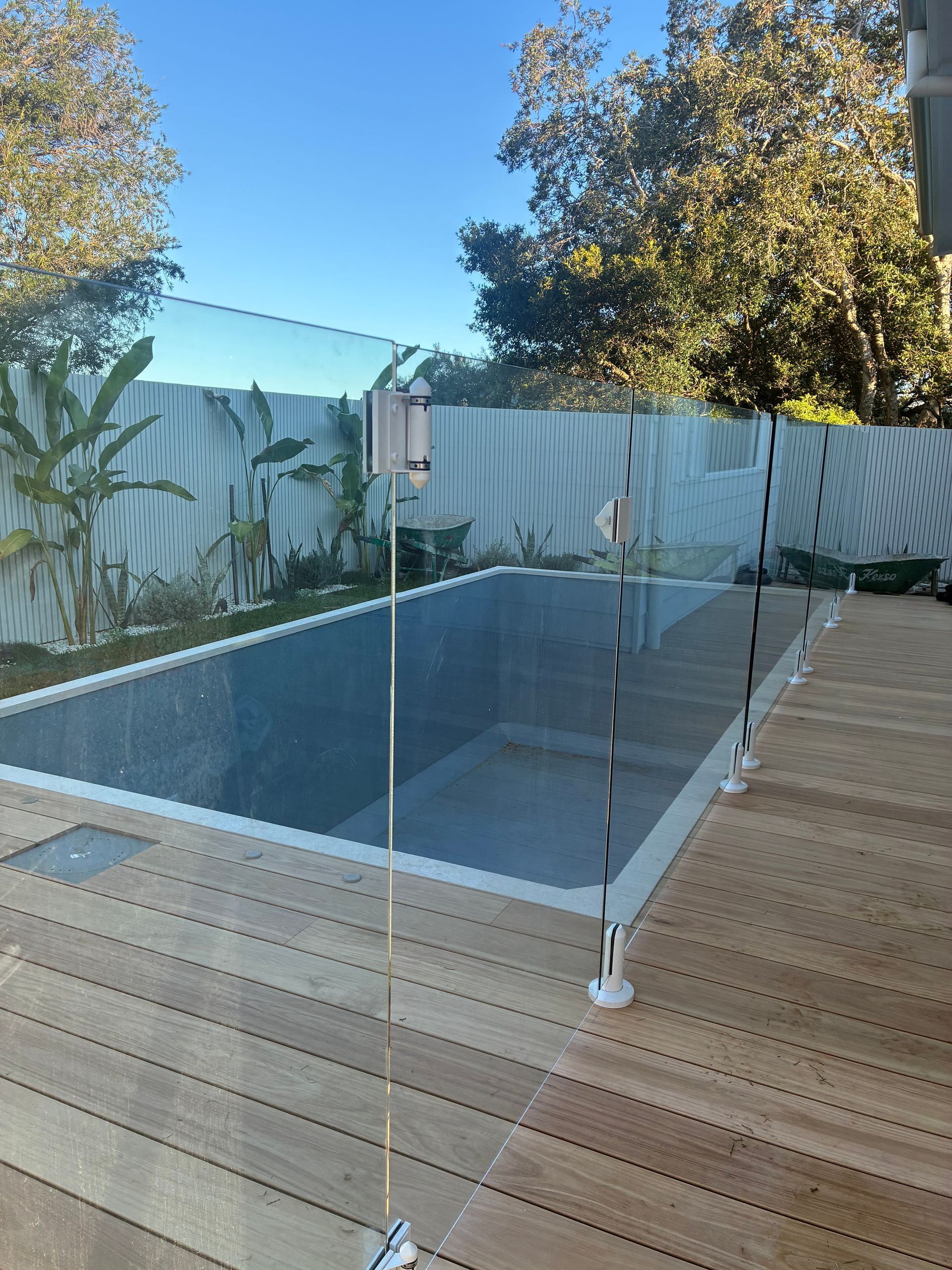 Modern backyard deck with a glass-railed pool and trees in the background — Kracken Windows and Doors In Terrey Hills, NSW