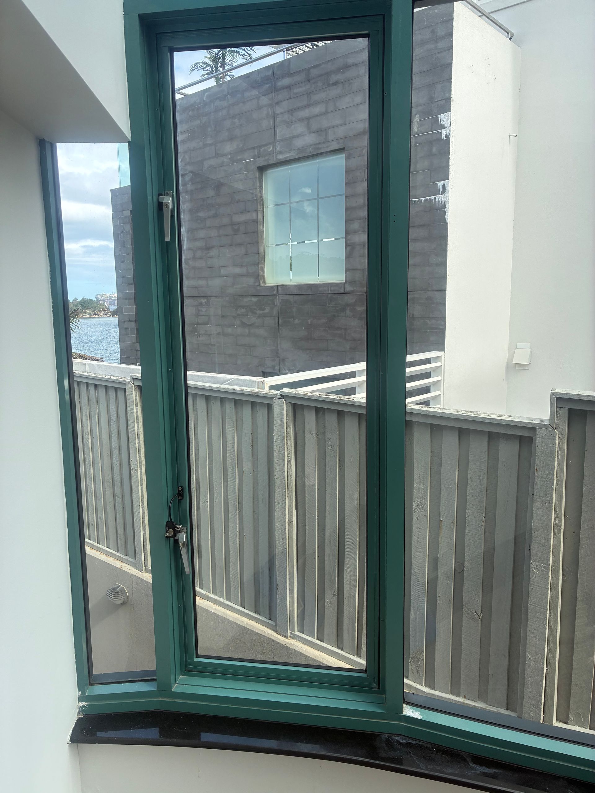 Balcony view through a green-framed window toward neighboring buildings and a fence — Kracken Windows and Doors In Terrey Hills, NSW