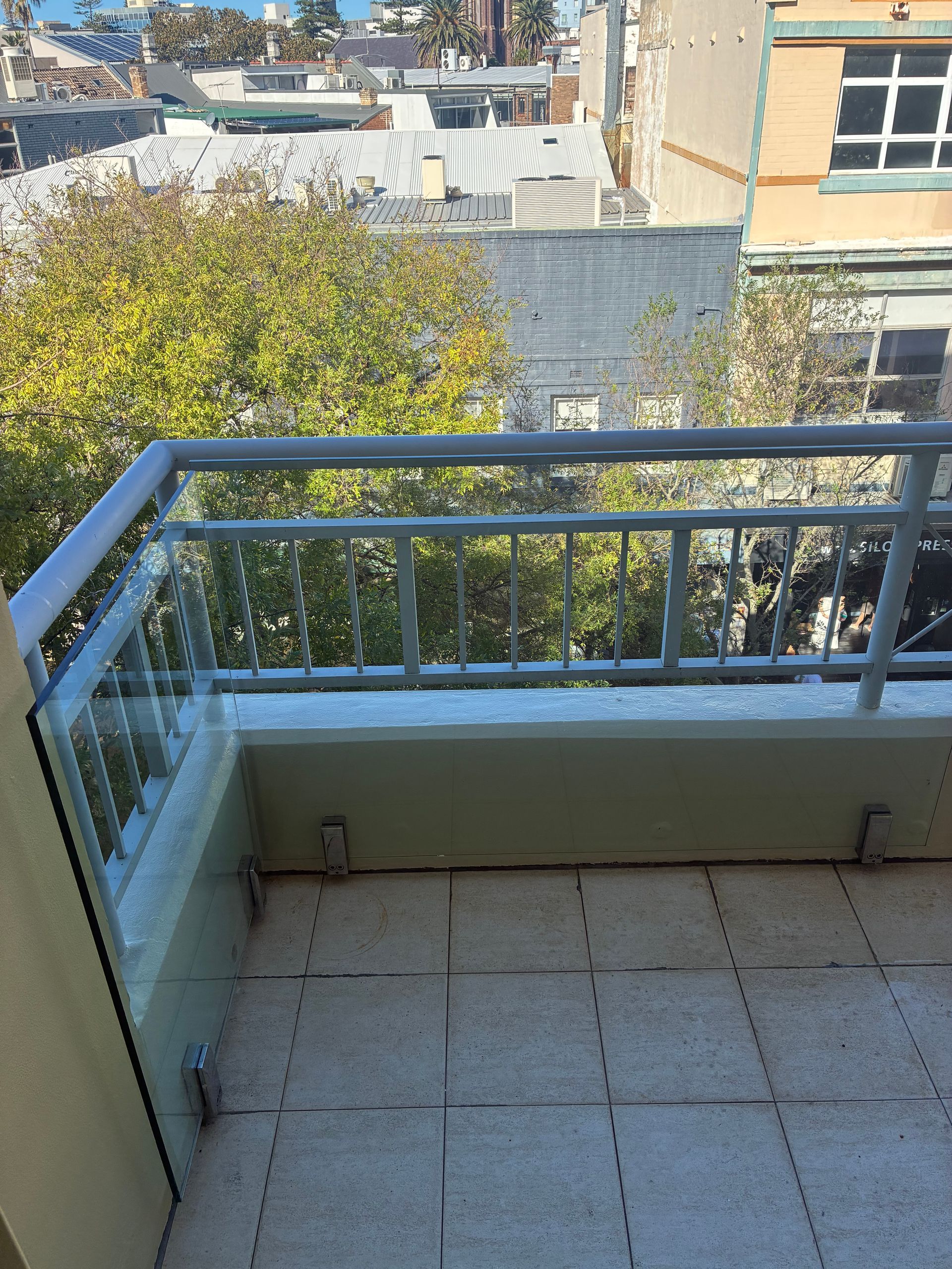 Small balcony with metal railing, tiled floor, and a view of nearby rooftops and trees. — Kracken Windows and Doors In Terrey Hills, NSW