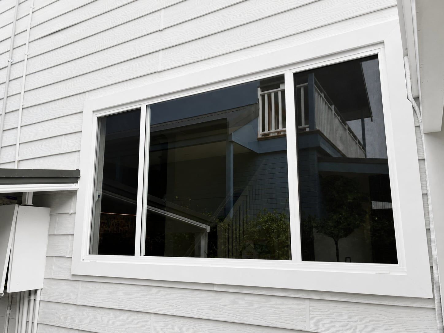 White house exterior with a large three-panel window and dark reflections of the porch and sky — Kracken Windows and Doors In Terrey Hills, NSW