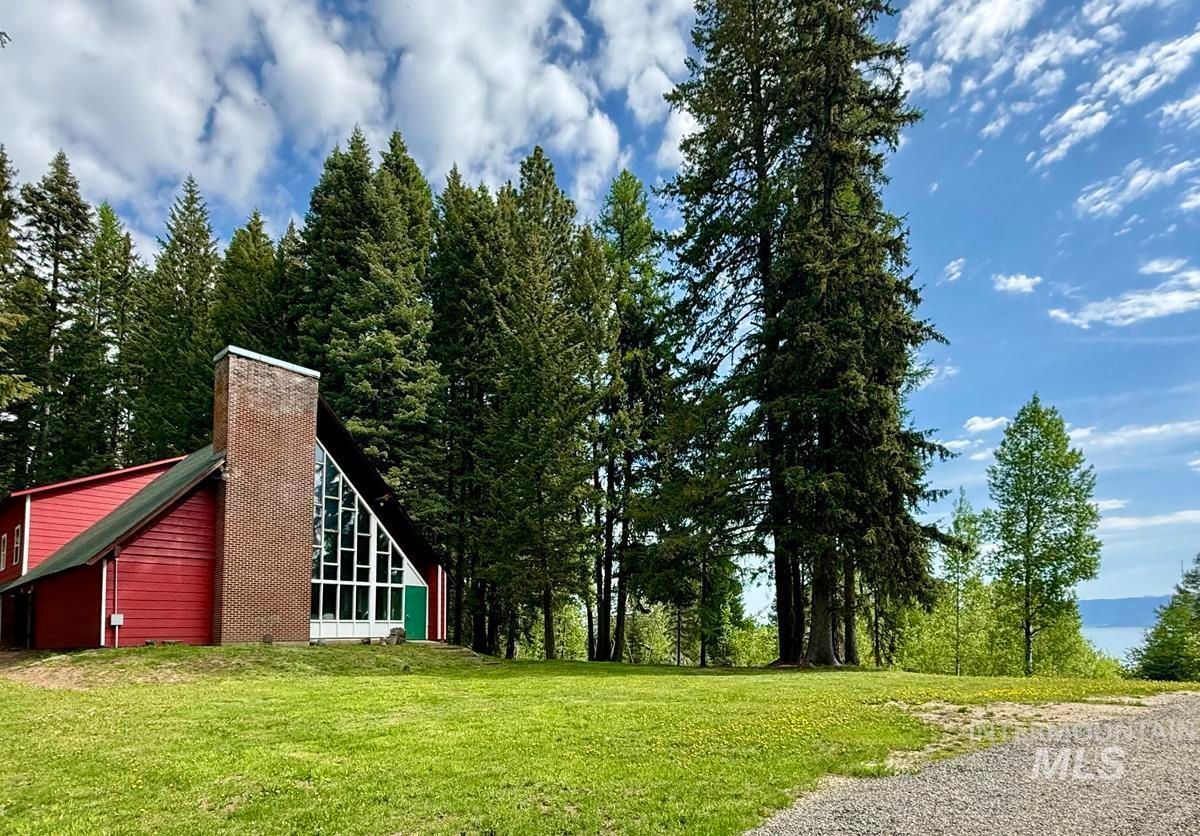 Red cabin with tall trees on a grassy clearing under a blue sky