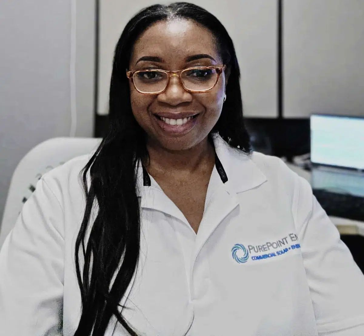 Smiling woman in white PurePoint Energy medical coat and glasses seated in an office
