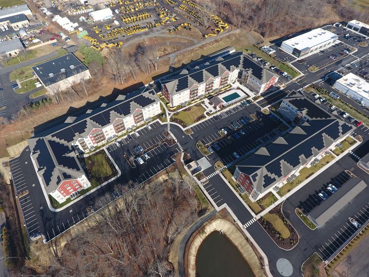 Aerial view of a large residential complex with rows of buildings, parking lots, and a pond.