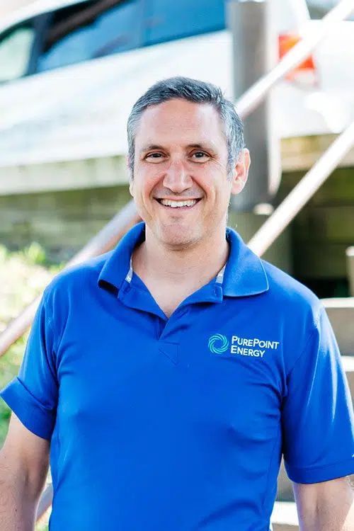 Smiling man in a blue PurePoint Energy polo shirt standing outdoors in front of a modern building