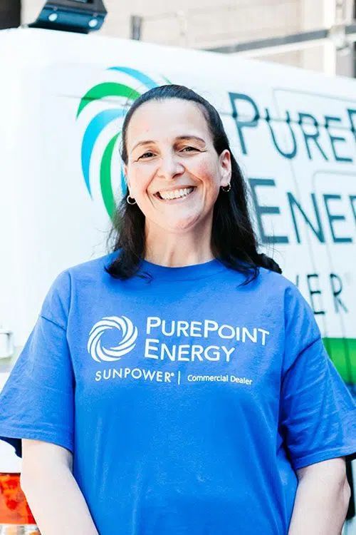 Woman in blue PurePoint Energy T-shirt standing and smiling in front of a branded vehicle.