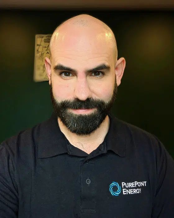 Smiling bald man with beard wearing a black PurePoint Energy polo shirt against a blurred dark background