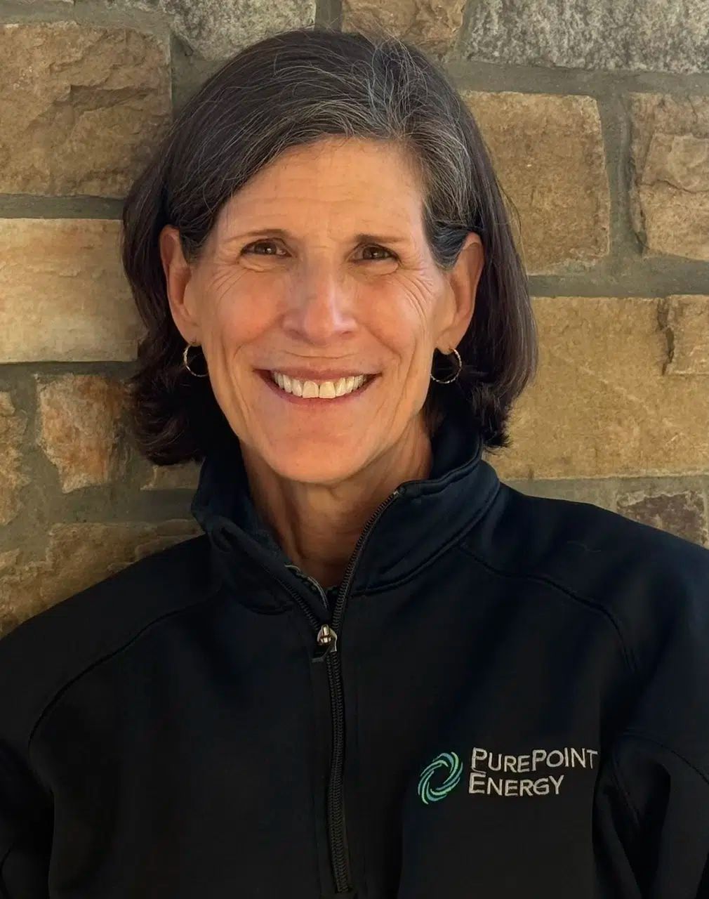 Woman smiling in a black PurePoint Energy jacket against a stone wall