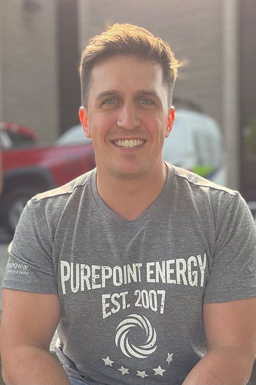 Smiling man in gray “PurePoint Energy” T-shirt outdoors in sunlight