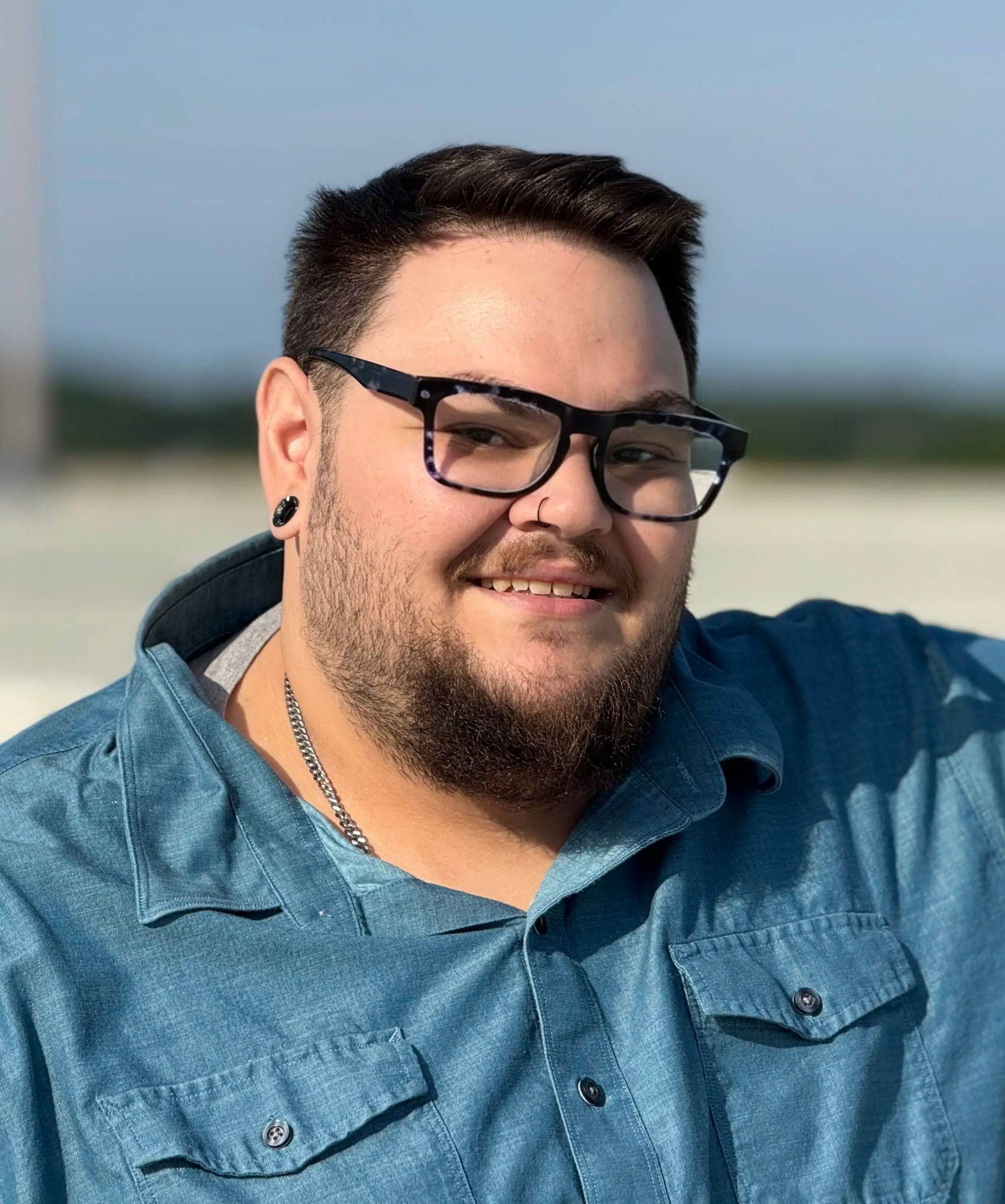 Smiling person in glasses and a blue PurePoint Energy shirt outdoors, with a blurred beach background