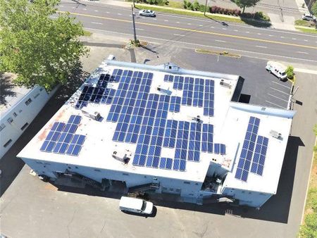 Aerial view of a building roof covered with blue solar panels beside a street and parked cars