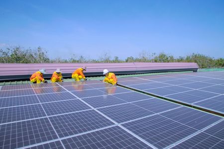 Workers in orange vests cleaning solar panels on a rooftop under a clear blue sky