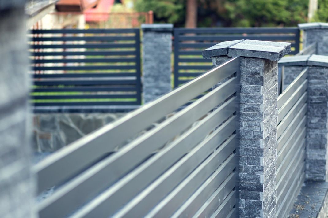 Gray and black modern fence with stone pillars in an outdoor setting.