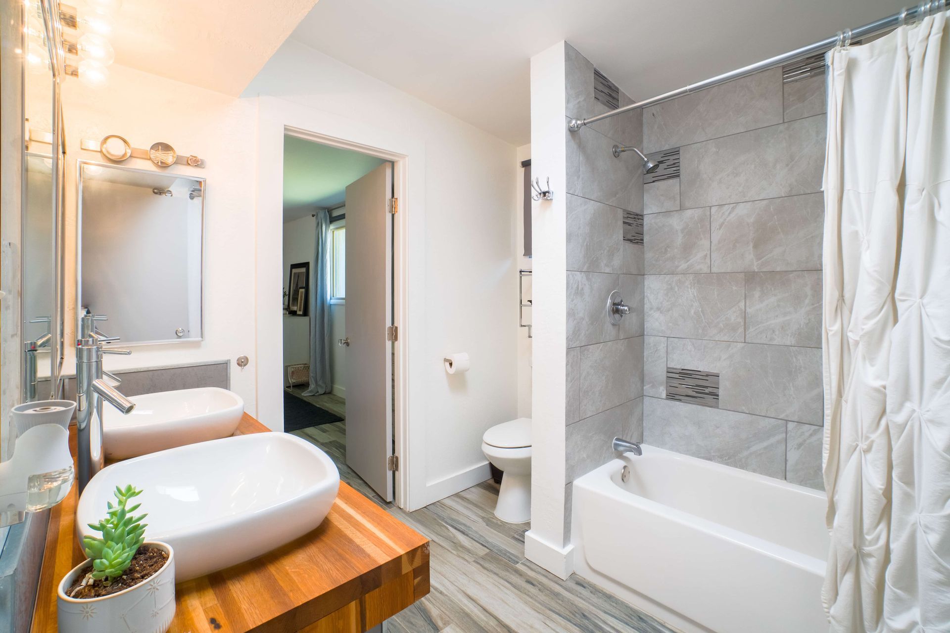 Modern bathroom with vessel sinks, tiled shower, and open doorway.