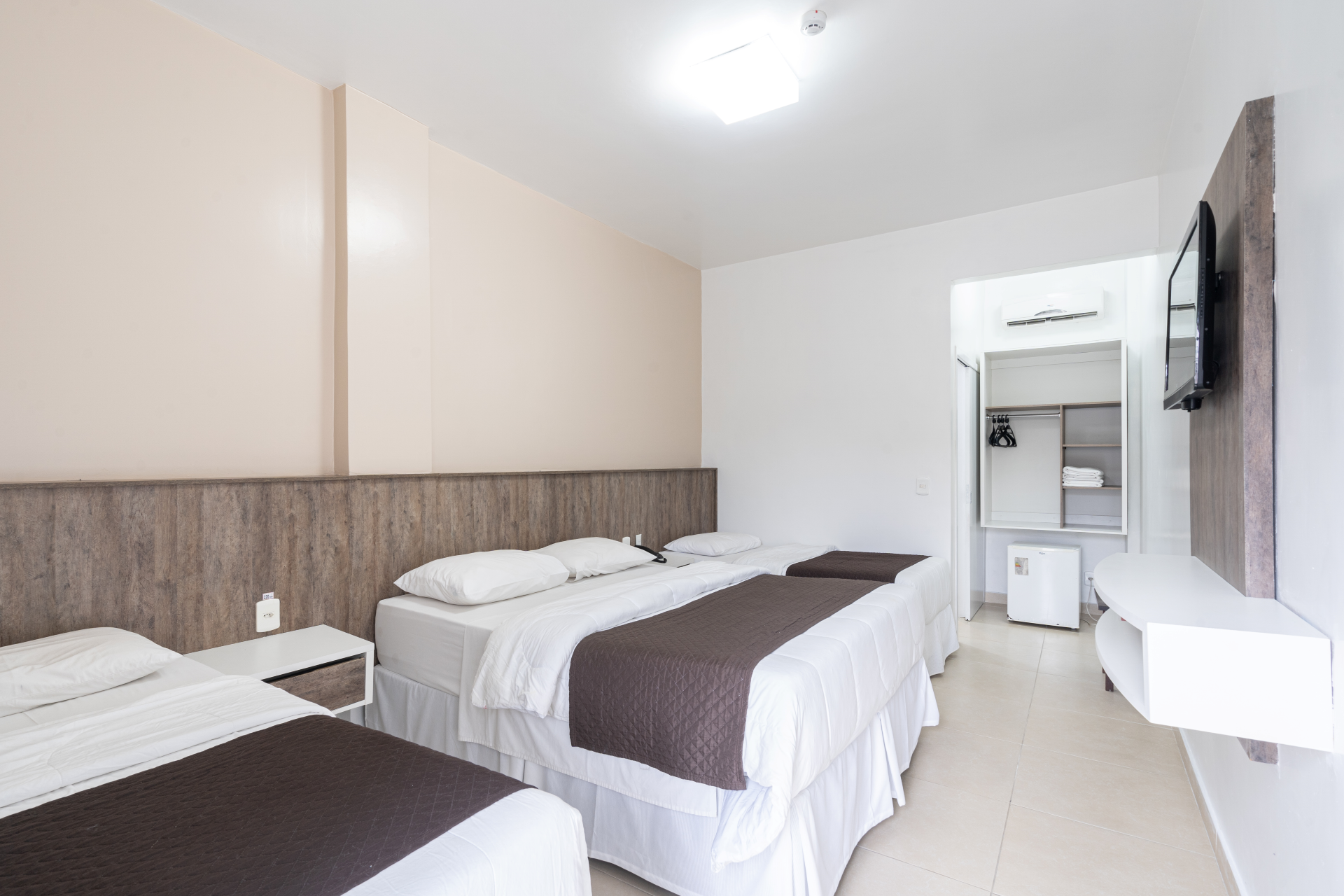 Um quarto de hotel com três camas e uma TV de tela plana.