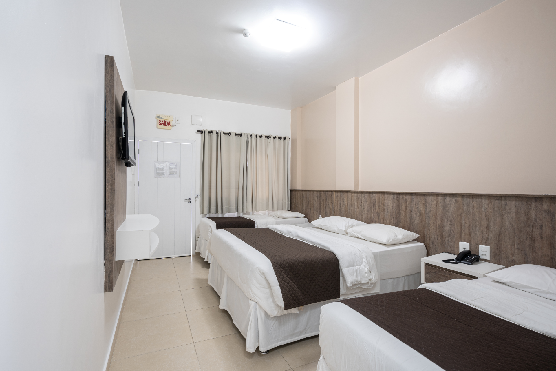 Um quarto de hotel com três camas e uma televisão.