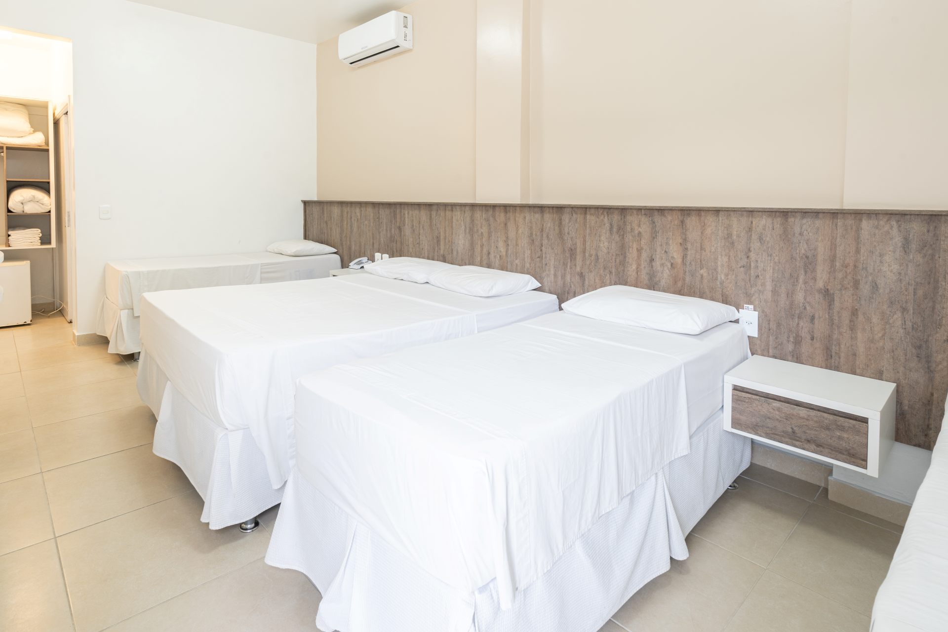 Um quarto de hotel com três camas e uma mesa de cabeceira.