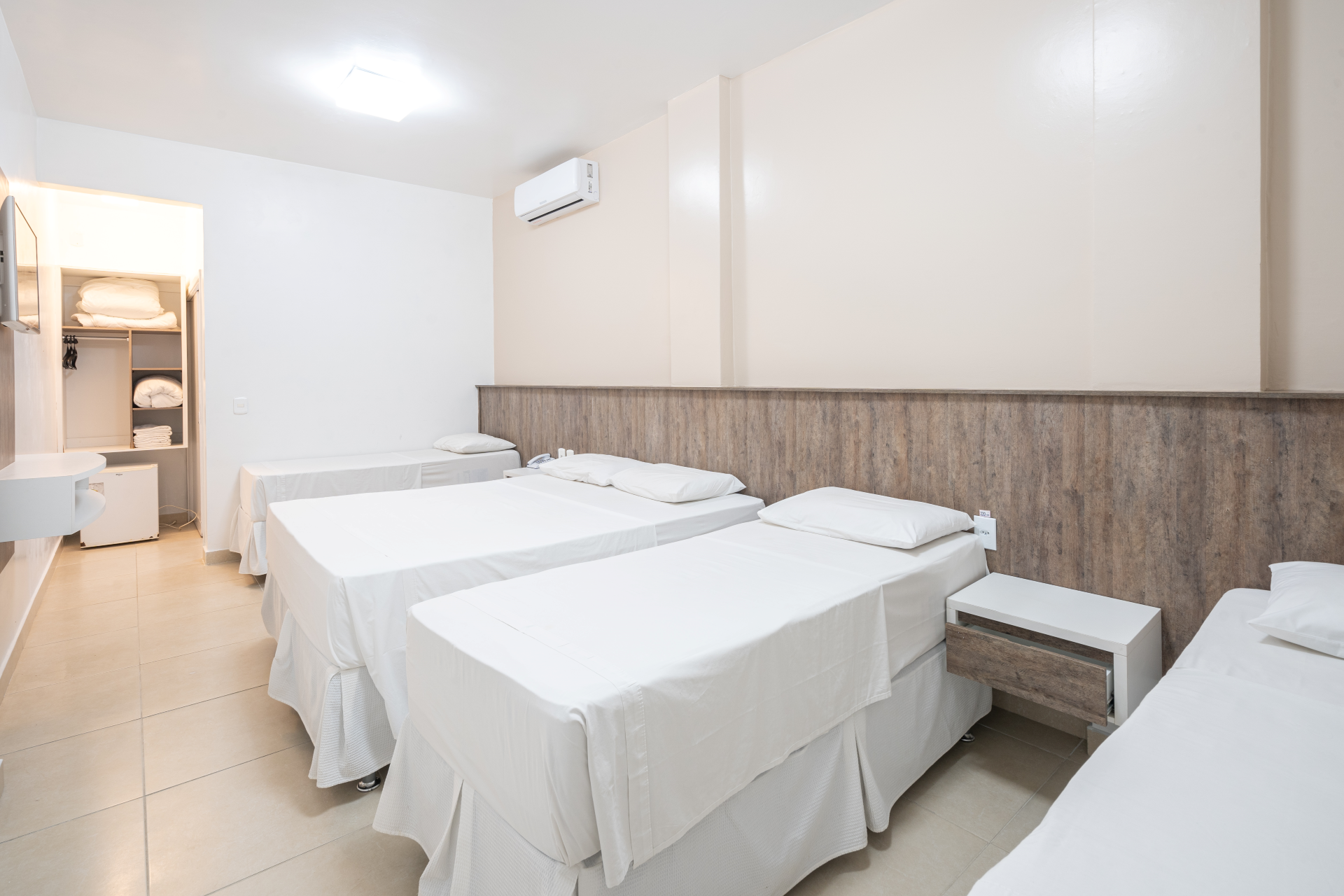Um quarto de hotel com três camas e um armário.
