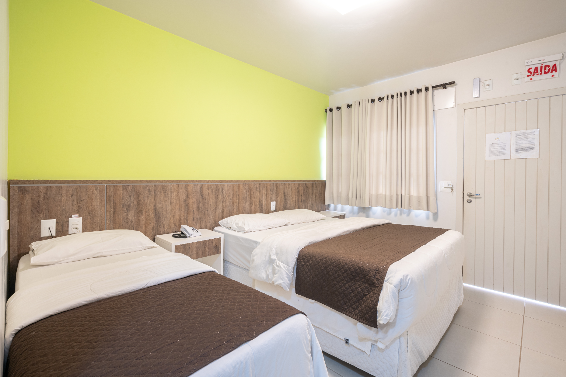 Um quarto de hotel com duas camas e uma parede amarela.