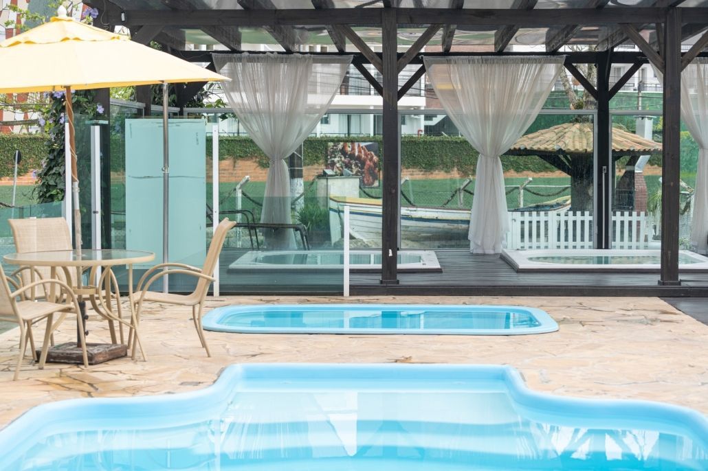 Há uma piscina com uma mesa e cadeiras ao fundo.