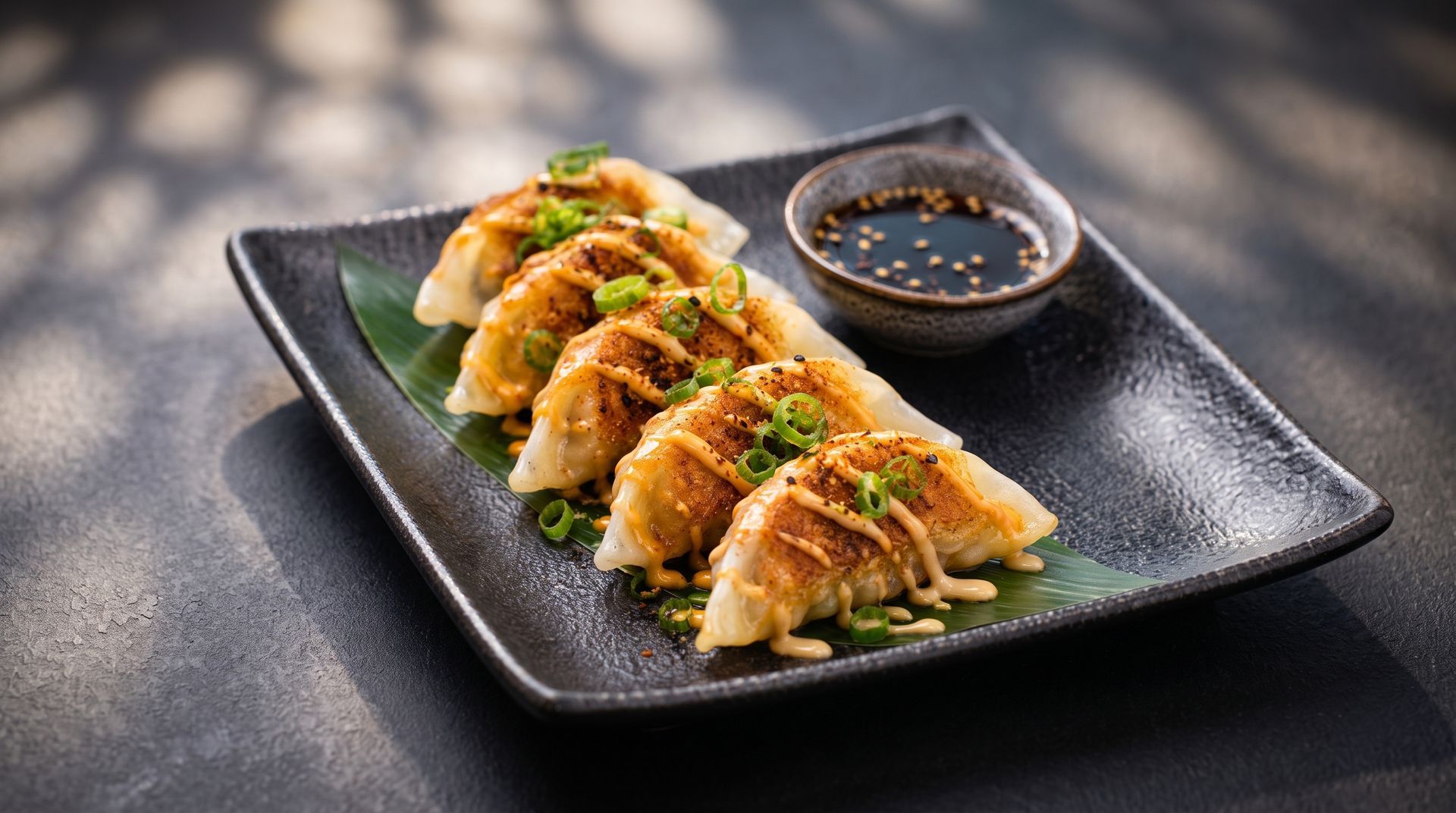 Gyoza dumplings on a black plate with chopped garnish and dipping sauce in a small bowl