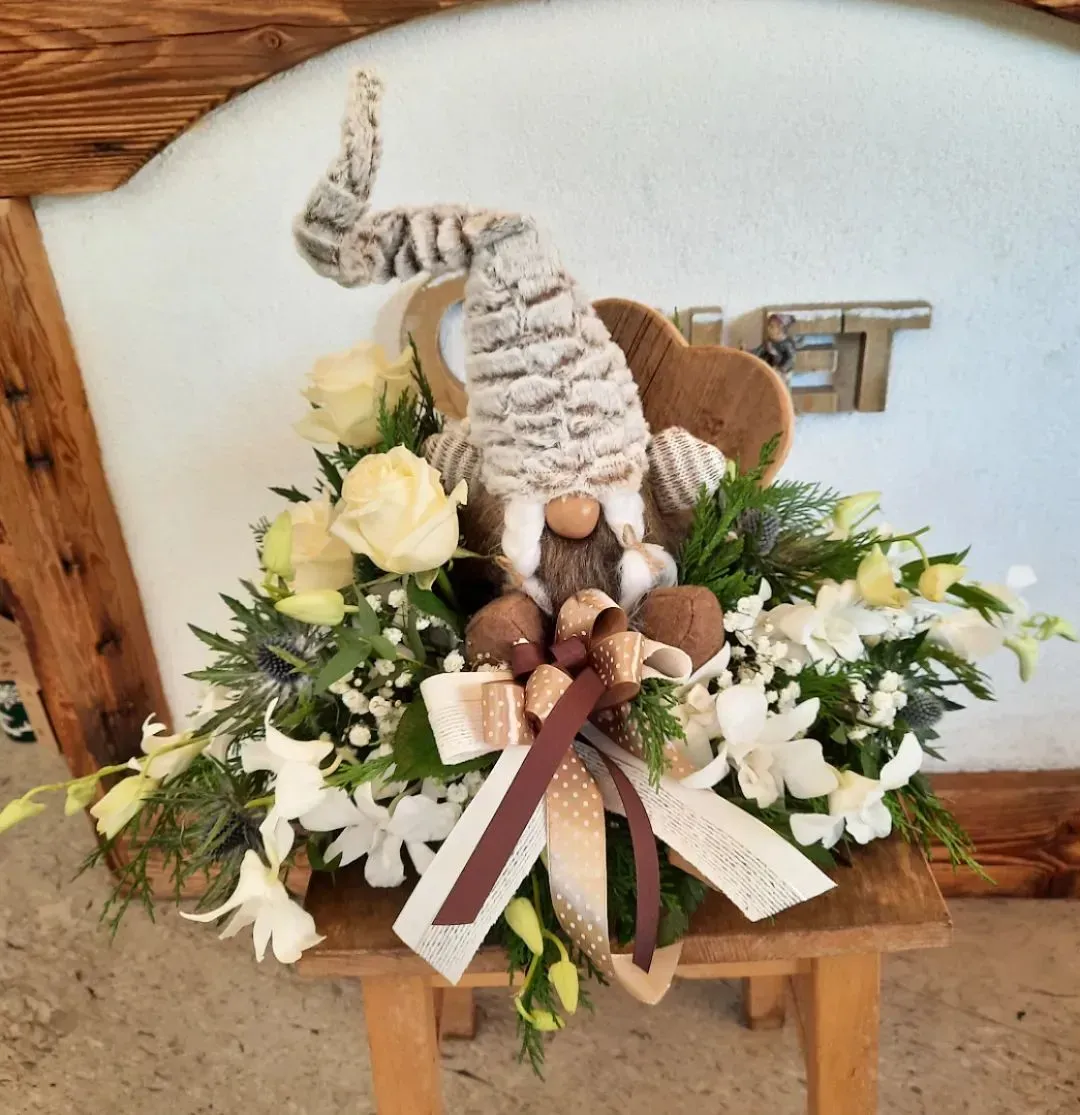 Composizione floreale a forma di coniglietto pasquale con fiori bianchi, funghi e nastro su una panchina di legno.
