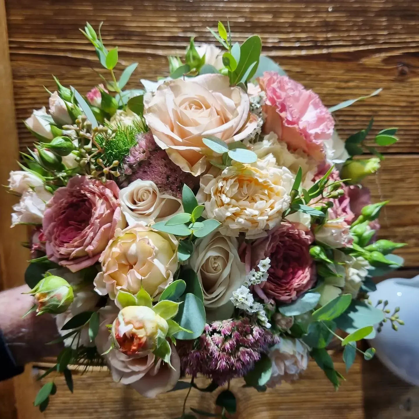 Bouquet dai toni pastello di rose rosa, crema e pesca con verde su un tavolo di legno.