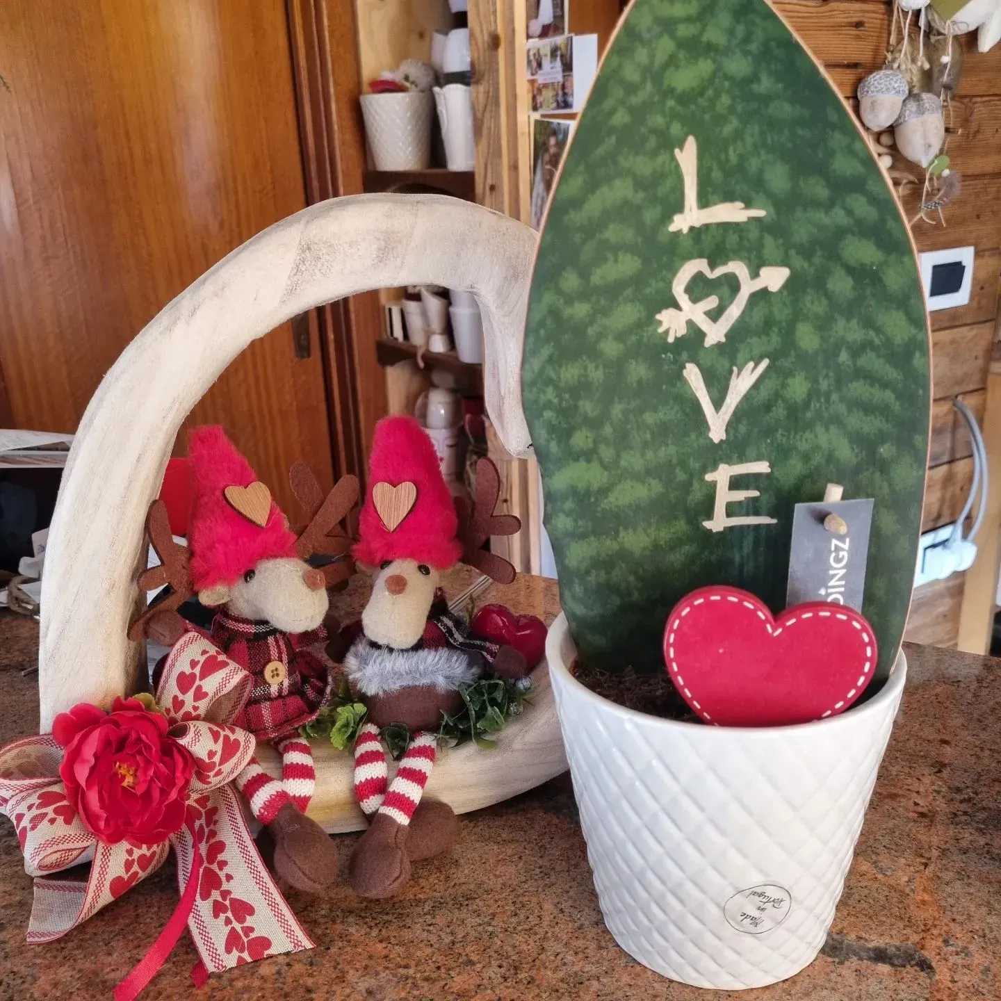 Decorazione da tavolo per San Valentino con due statuine di gnomi, decorazioni a forma di cuore e un cartello con una foglia verde con la scritta LOVE.