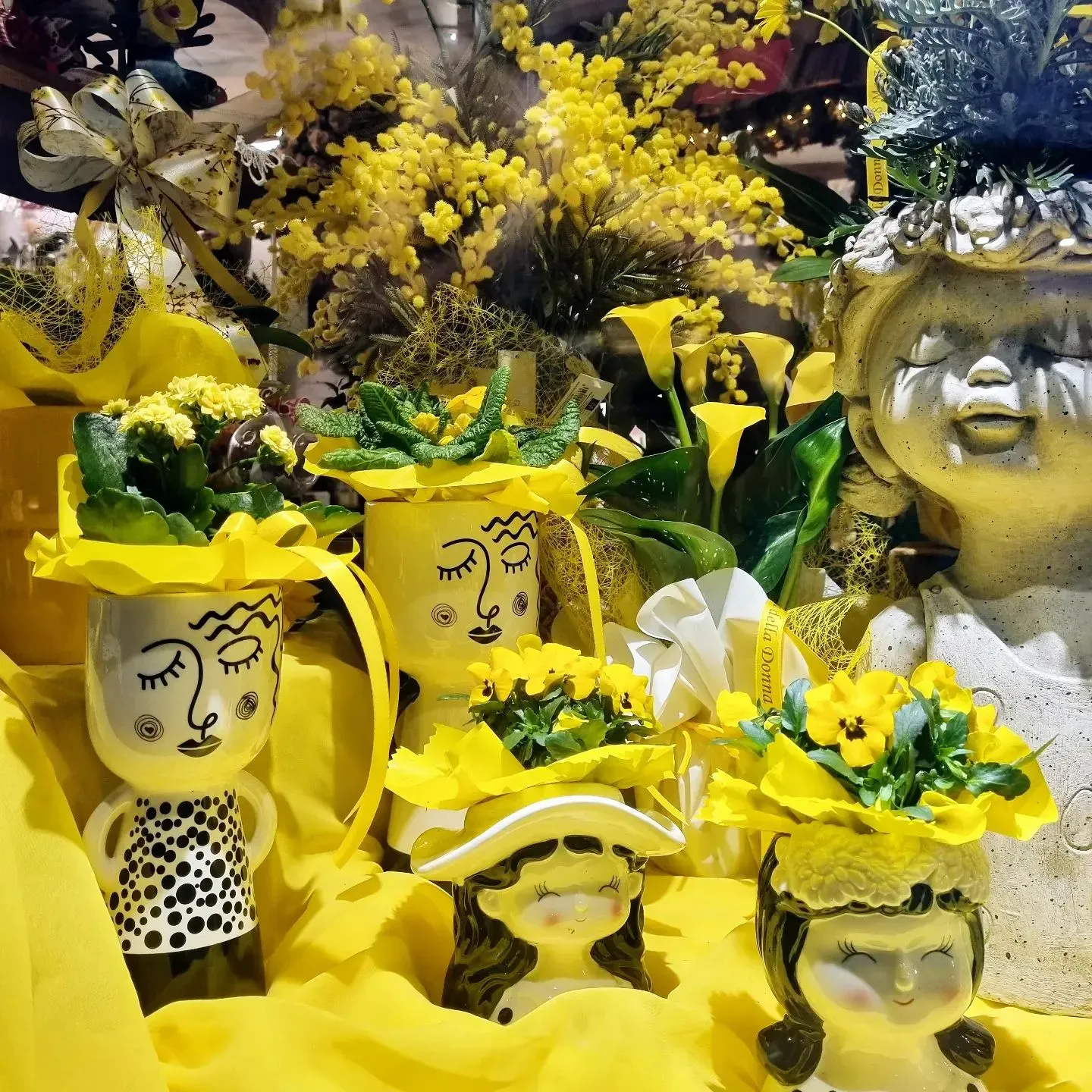 Composizione floreale gialla con volti e cappelli decorati tra i fiori