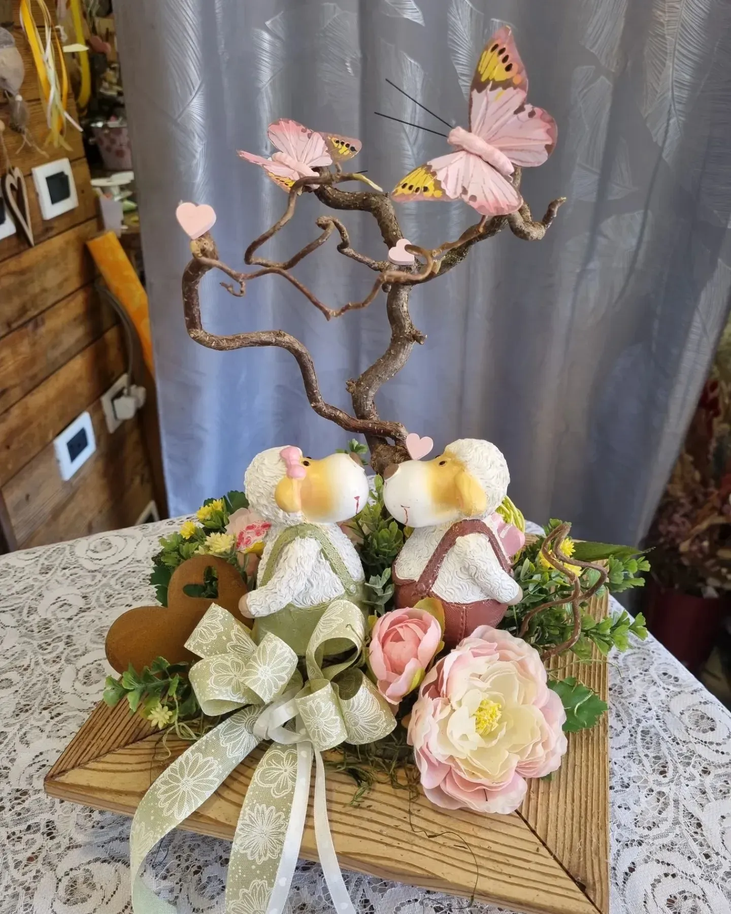 Composizione floreale decorativa con farfalle rosa e nastro su base di legno.