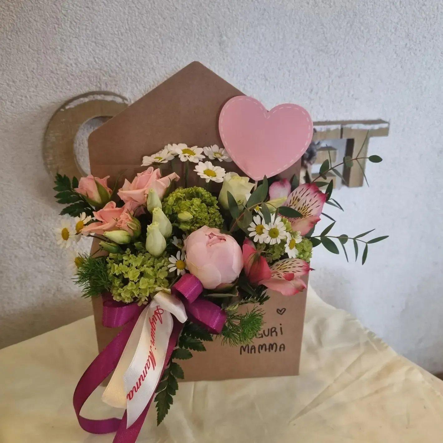 Scatola regalo floreale rosa e bianca con decorazione a cuore e nastro su un tavolo