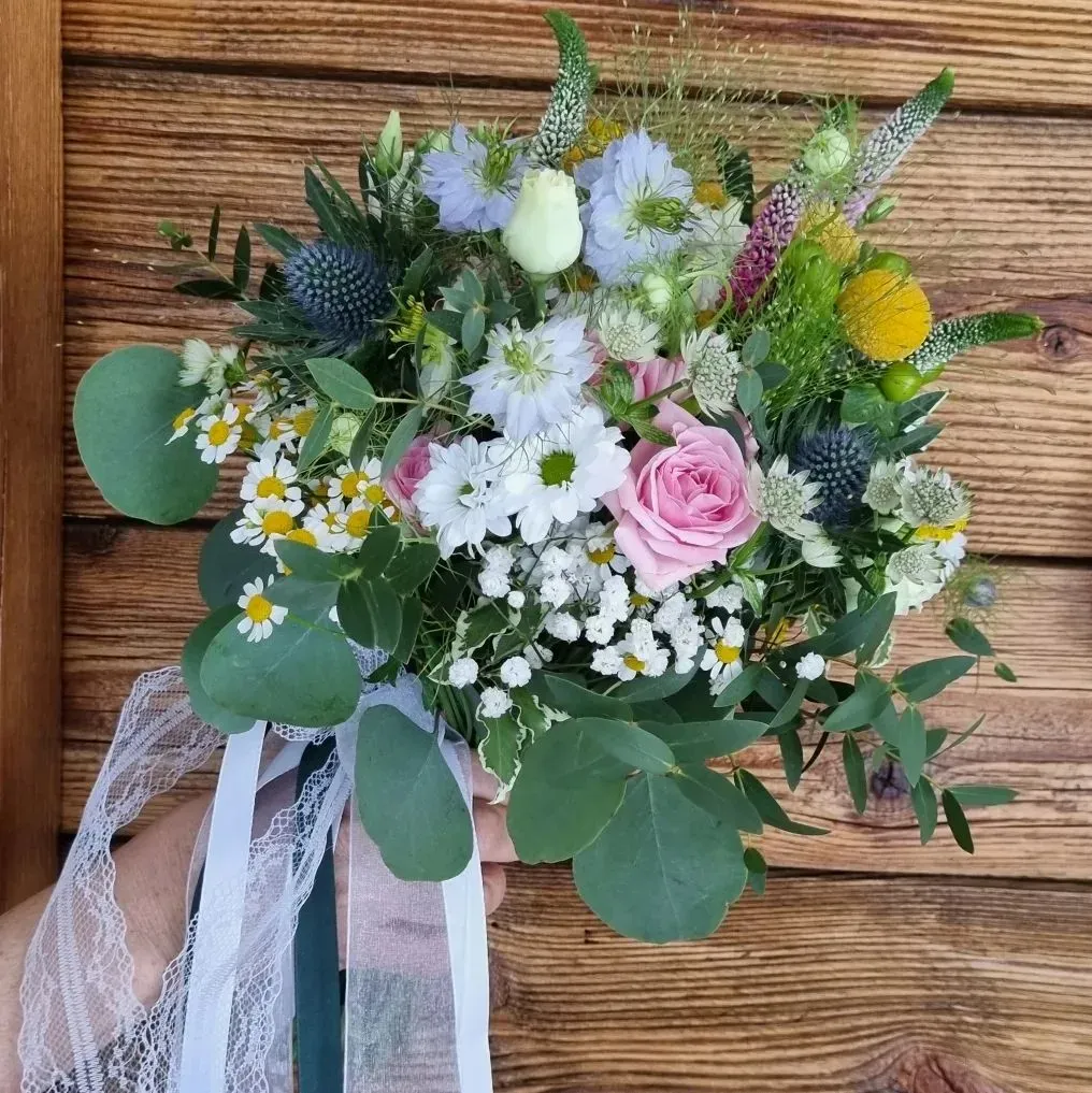 Bouquet di fiori di campo dai colori pastello con rosa rosa, margherite bianche e nastro su una superficie di legno.