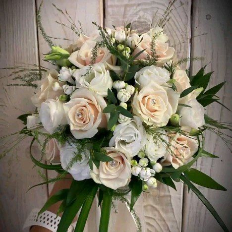 Bouquet di rose bianche e rosa pallido con fogliame verde, legato con un nastro.
