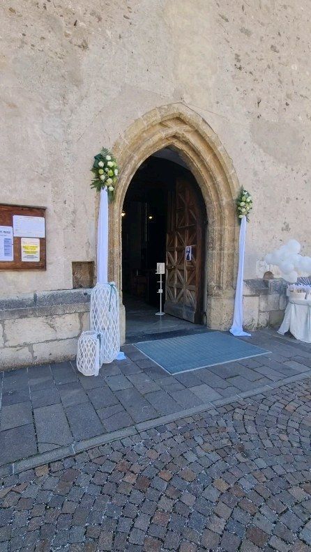 Portale in pietra della chiesa con arco a sesto acuto, decorazioni floreali e sentiero lastricato all'esterno.